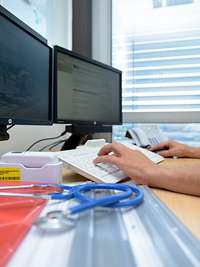 Zentrales Klinisches Management am Bundeswehrkrankenhaus Person bedient eine Computertastatur vor zwei Monitoren mit einem daneben liegendem Stetoskop