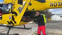 Ein Mann in Rettungsdienstkleidung schiebt eine Trage in einen Hubschrauber