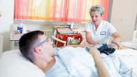 Krankenpflegerin führt am Bett eines Patienten eine Schmerztherapie durch
