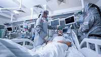 Patient wird in der Infektiologie von zwei Kranken- und Gesundheitspflegern versorgt