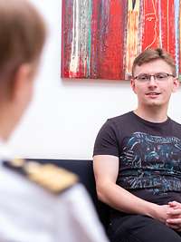 Eine Ärztin sitzt auf einer Couch im Gespräch mit einem Patienten