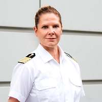 Eine Soldatin in einem weißem Hemd und Jacke steht vor einer Wand