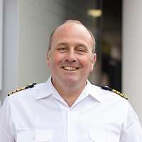 Ein Soldat in einem weißem Hemd steht vor einer Wand