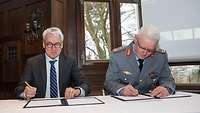 Ein Soldat und ein Mann sitzen nebeneinander und unterzeichnen ein Dokument