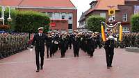 Mehrere Soldaten mit Musikinstrumenten marschieren auf einen rot gepflasterten Platz