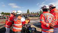 Vier Rettungskräfte warten mit ihrer Ausrüstung in der Nähe eines verunfallten Autos.