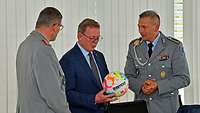 Drei Personen stehen zueinander. Die Person in der Mitte hält einen Fußball in der Hand