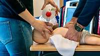Eine Person beatmet eine Kleinkindpuppe während die Andere eine Herzdruckmassage durchführt