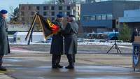 Ein Soldat übergibt eine deutsche Truppenfahne an einen anderen Soldaten