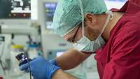 Ein Arzt in roter OP- Bekleidung führt ein Laryngoskop zur Intubation eines Patienten ein