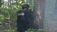 Ein Polizist hinter einem Baum in Deckung mit einer Maschinenpistole im Anschlag