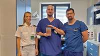 Eine Frau und zwei Männer in Krankenhauskleidung präsentieren das Resektat.