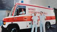 Der erste Notarztwagen der Bundeswehr. Man sieht zwei Rettungssanitäter nebem dem Wagen stehen