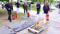 Eine Frau löscht ein Feuer mit einem Feuerlöscher. Mehrere Personen stehen dabei