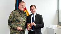 Ein Soldat und ein zivil gekleideter Mann stehen nebeneinander und präsentieren einen Coin und Wappen