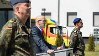 Ein Mann steht an einem Rednerpult und links und rechts von ihm stehen 2 Soldaten