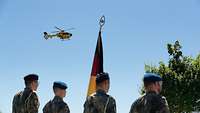 Ein gelber Hubschrauber in der Luft. Im Vordergrund 4 Soldaten