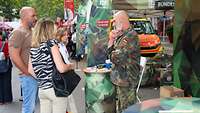Ein Soldat informiert Besucher am Informationstand. Im Hintergrund ist ein Rettungswagen zu sehen.