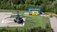 Mehrere Rettungsfahrzeuge warten an einer Zufahrt im Vordergrund ein Transporthubschrauber des Typs CH 53