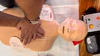 Man sieht Hände die eine Herzdruckmassage an einer Reanimationspuppe durchführen