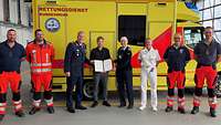 Acht Personen stehen mit der Rezertifizierungsurkunde vor einem Rettungswagen der Bundeswehr.